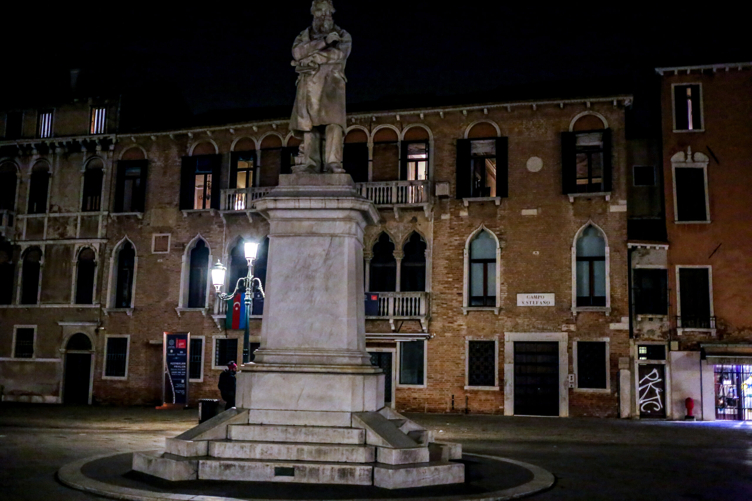 Campo Santo Stefano in Venice late at night, the marble monument to Niccolo Tommaseo lit by a street lamp in front of a Gothic palazzo