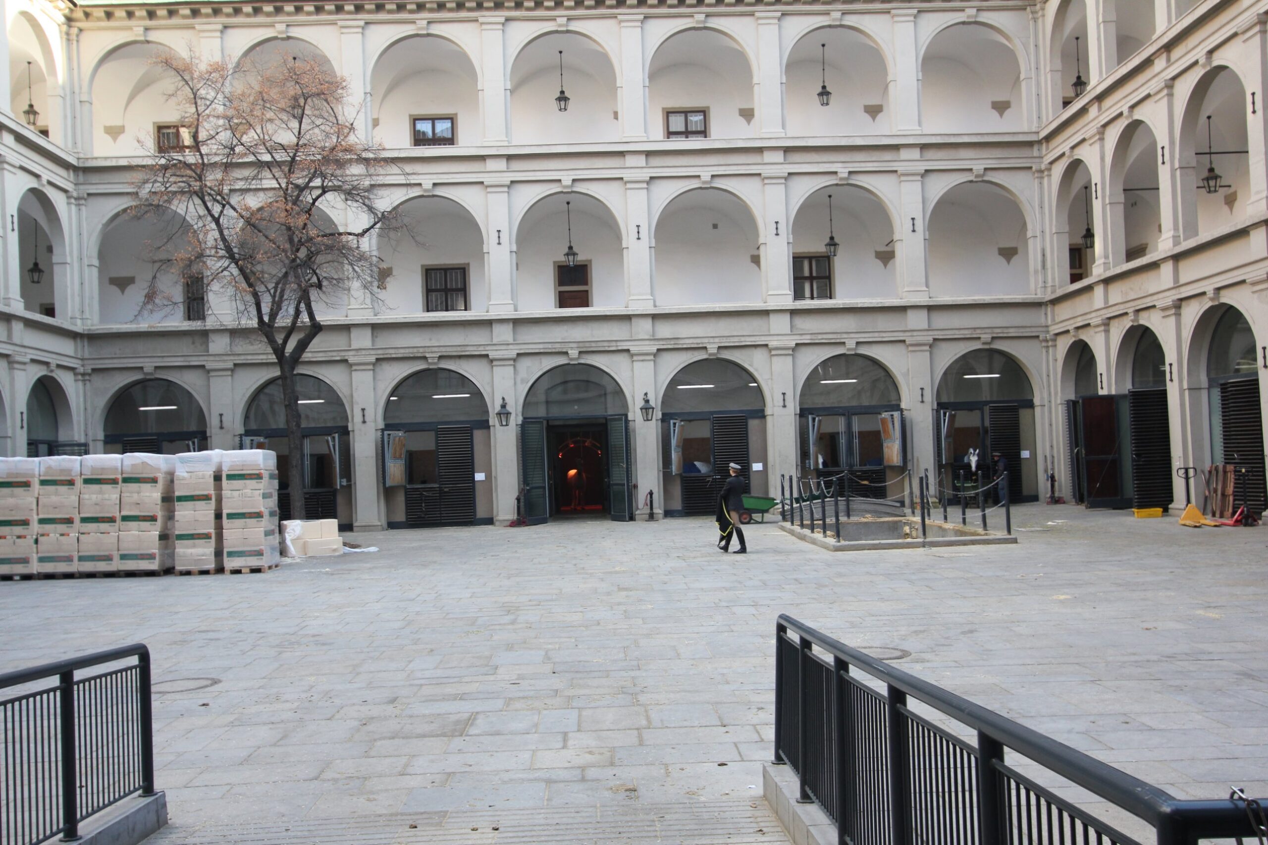 The Renaissance arcaded courtyard of the Stallburg in Vienna, with the open stable doors of the Lipizzaner stallions on the ground floor and a groom crossing the yard